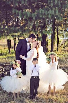 a bride and groom kissing in front of their children wearing tutu skirts with flower crowns