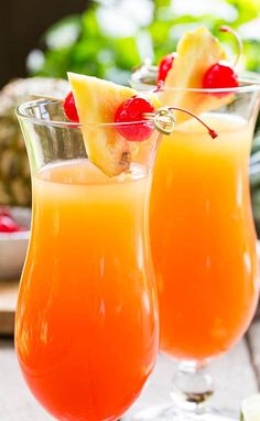 two glasses filled with orange juice and garnished with pineapple on the rim