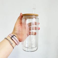 a hand holding a glass jar with a straw in it and a pink strap around the wrist