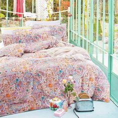 a bed covered in a colorful paisley print comforter next to a green wall and window