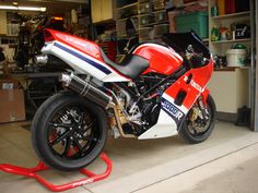 a red and white motorcycle parked inside of a garage next to a metal shelf filled with tools