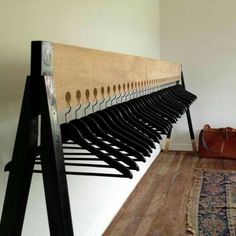 a wooden rack with black clothes hanging from it's sides on a wall next to a rug