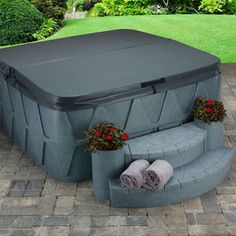 an outdoor hot tub sitting on top of a brick patio next to flowers and towels