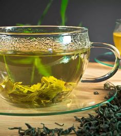 a glass cup filled with green tea sitting on top of a table next to some flowers