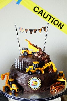 a birthday cake with construction vehicles on top and caution tape in the air above it