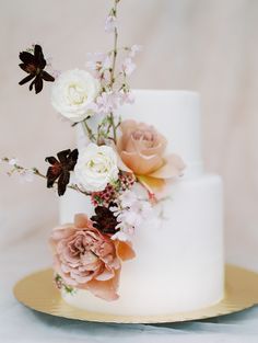 a white wedding cake with flowers on the top and bottom layer, sitting on a gold plate