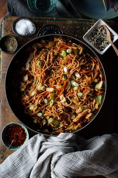 a pan filled with noodles and vegetables on top of a wooden table next to other dishes