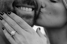 a man and woman kissing each other with their engagement rings on their fingers in black and white