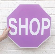 a person holding up a pink and white sign that says shop on the side of a brick wall