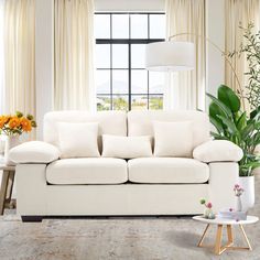 a living room with a white couch and table in front of a window filled with flowers