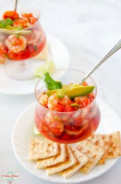 two small bowls filled with food on top of a white plate next to crackers