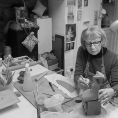 a woman sitting at a table working on something with scissors and paper in front of her