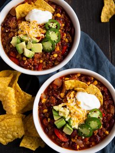 two white bowls filled with chili and tortilla chips on top of a blue napkin