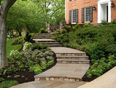 steps leading up to the front door of a brick house with trees and bushes around them