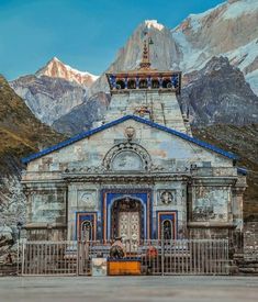 an old church in the mountains with snow on the mountain behind it and a blue roof