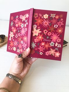 a person holding up a pink book with flowers on it and the word diary written in large letters