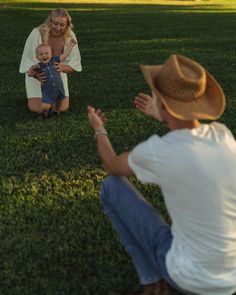 two women and a baby are sitting in the grass, one is holding her hands out