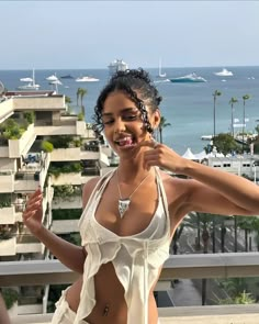 a woman in a bathing suit standing on a balcony next to the ocean and buildings