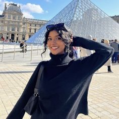 a woman standing in front of a pyramid with her hand on her head and wearing a black sweater