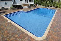 an empty swimming pool in the middle of a brick patio area with a deck and chairs