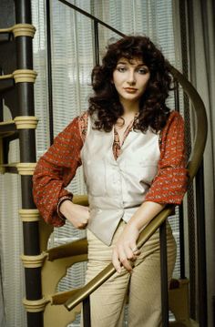 the woman is posing on the stairs with her hand in her pockets and wearing a red shirt