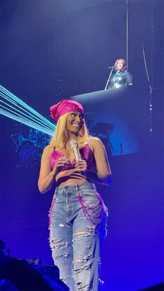 a woman in ripped jeans and pink headband holding a microphone while standing on stage