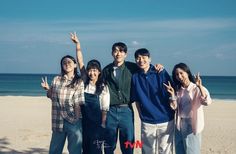 a group of people standing next to each other on top of a sandy beach with the ocean in the background