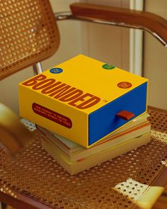 a stack of books sitting on top of a wooden chair next to a yellow box