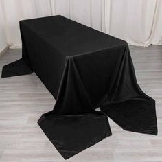 a black table cloth on top of a wooden floor next to a white wall with curtains