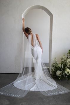 a woman in a wedding dress is standing with her back to the camera and veil over her head