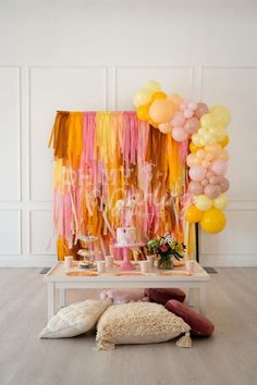 a table topped with cake and balloons in front of a wall filled with streamers