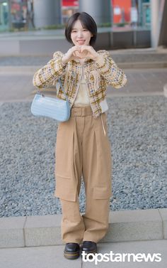 a woman standing in front of a building making a heart sign with her hands while holding a blue purse