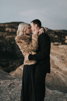 a man and woman kissing on top of a mountain