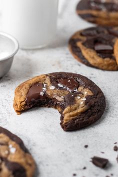 chocolate chip cookies with one broken in half and the other partially eaten, sitting on a white surface next to a cup of coffee