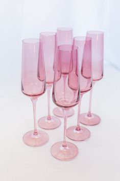 six pink wine glasses lined up on a white table top with one empty glass in the middle