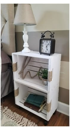 a small white shelf with a clock on top of it next to a lamp and books