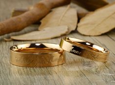 two gold wedding rings sitting on top of a wooden table next to leaves and fallen leaves