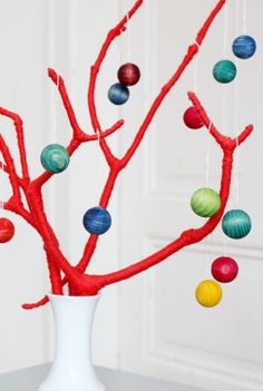 a white vase filled with colorful balls on top of a table next to a tree