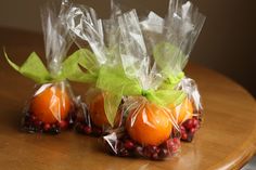 three oranges wrapped in plastic sitting on top of a wooden table with pomegranate