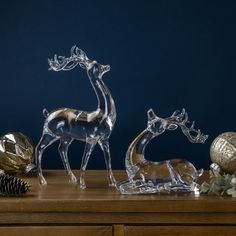 two glass deer figurines sitting on top of a wooden table next to pine cones