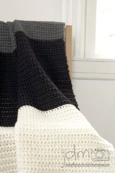 black and white crocheted blanket sitting on top of a bed next to a window