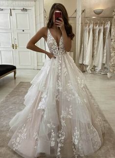 a woman taking a selfie while wearing a wedding dress with white flowers on it