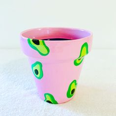 a pink flower pot with green leaves painted on the outside and inside, sitting on a white surface