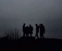 silhouettes of people standing on top of a hill under an airplane in the sky