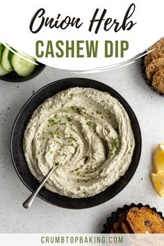 a bowl filled with cashew dip surrounded by cucumbers and crackers on a white surface