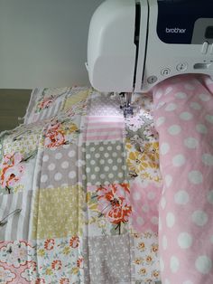 a sewing machine is on top of a patchwork quilted bedding with pink and white flowers