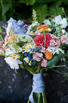 a bouquet of colorful flowers sitting on top of a stone wall with greenery behind it