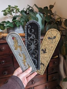 three decorative bookmarks are held in front of a dresser