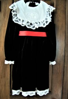 This pretty long sleeve special occasion dress has a lace trimmed collar with an oval flower design and 5 tiny white pearls in the center of the flower.  The dress also has a white lace trimmed hem and sleeves and a red satin sash that ties in the back.  The sash is held in place by a satin loop on each side. The dress opens with 5 black buttons on the back.  This dress is in excellent condition with no stains, rips or color wear.  It comes from a smoke free home and was stored between tissue pa Long Sleeve Winter Costume Dress, Winter Costume Dress With Long Sleeves, Winter Costume Long Sleeve Dress, Winter Long Sleeve Costume Dress, Long Sleeve Victorian Dress For Winter Costume, Vintage Victorian Long Sleeve Dress For Fancy Dress, Vintage Long Sleeve Victorian Dress For Fancy Events, Long Sleeve Victorian Dress For Fall Costume Party, Long Sleeve Dresses For Fancy Dress In Fall