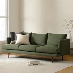 a green couch sitting on top of a wooden floor next to a white vase filled with flowers